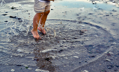 Autumn seashore. A child girl jumps barefoot through the sea puddles. Children's rest. Happy...