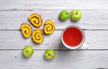 top view of  delicious biscuit rolls with apricot jam, green apples and cup of red drink on a white rustic wooden table