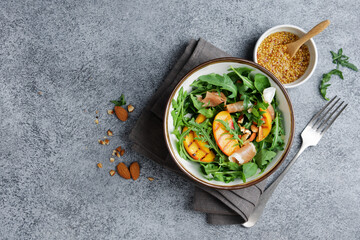 Grilled peach salad with rucola, jamon and almonds. Bowl with fruit salad on gray marble background