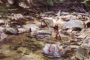 Happy little girl have fun in clear mountain rocky creek at summer forest. Beautiful natural day light. Adventure