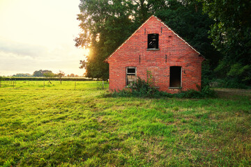 abandoned damaged shed made of red bricks on a green meadow against evening sky