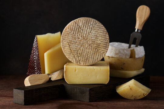 Set of hard cheeses gruyere and manchego on cutting board on dark background