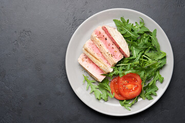 Tuna steak with arugula and tomato. Black slate background with copy space