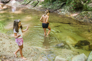 Fototapeta premium Happy children have fun by mountain creek at summer forest. Natural day light. Adventure