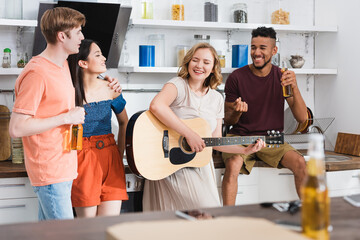 Obraz premium selective focus of young woman playing guitar for excited multicultural friends