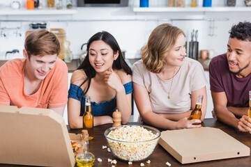 multicultural friends talking near popcorn, beer and pizza boxes during party