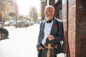 Positive elderly gentleman posing with a longboard