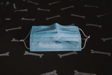 Una mascarilla quirúrgica azul sobre un fondo con un patrón de huesos para Halloween