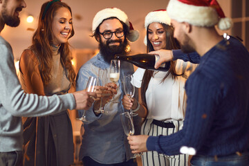 Young man pouring champagne into his friends' glasses at Christmas or New Year Party