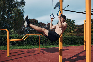 Young shirtless man bodybuilder doing L-Sit during his workout in a modern calisthenics street workout park