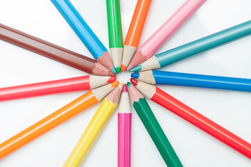 Fototapeta premium Colored pencils on a white background, pointing at the center of the frame.