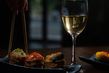  Close up shot of female hand enjoying Japanese cuisine various side dishes by chopstick, inari sushi set and white wine in restaurant 
