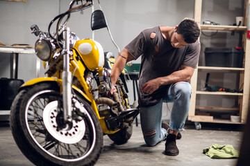 Fototapeta na wymiar A modern young man in a t-shirt and jeans is engaged in bike diagnostics in a repair shop or garage