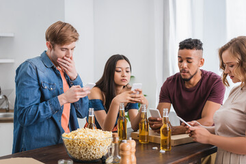 selective focus of multiethnic friends using mobile phones near beer and popcorn during party