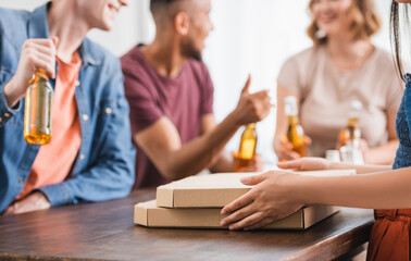 cropped view of woman near pizza boxes and multicultural friends with beer on background