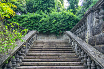 Ancient staircase are grey stone with stone balusters on a background of green vegetation