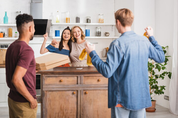 Fototapeta premium back view of multicultural friends holding pizza boxes and beer near women showing yeah gesture