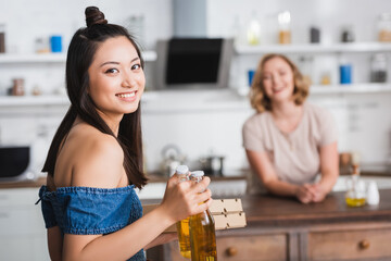 selective focus of excited asian woman holding beer and pizza boxes near friend on background