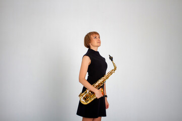Young woman with a saxophone in a black short dress in a photo studio