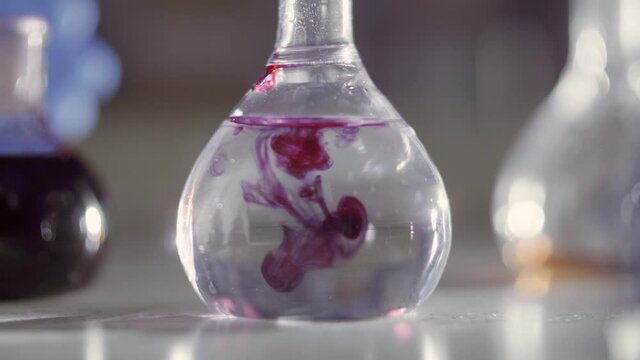 Flask with liquid in a chemical laboratory close-up. Workflow for adding a chemical component to a slurry. A drop of violet reagent falls into the clear reagent. Chemical experience.