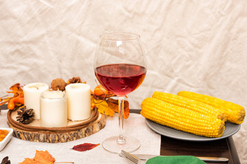 Glass of red wine on festive autumn holiday table setting with corn, fall decoration and candles. Thanksgiving family dinner.