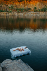 Woman sleeps on a mattress floating in the water near rocks.