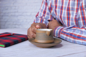 young man drinking tea with notepad and pencil on table 