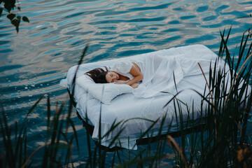 Woman sleeps on a mattress floating in the water among plants.