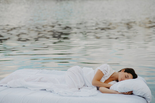 Woman sleeps on a mattress floating in the water.