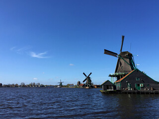 Fototapeta na wymiar dutch historic windmills near sea coast at blue sky, in Zaanse Schans, North Holland, Netherlands