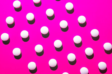 many white medical pills in a row on a pink background. pills cast a shadow. 
pill pattern. Copy space