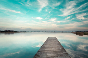 A wooden jetty towards water and clouds against a blue sky