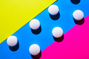many white medical pills in a row on a pink and blue and yellow background. pills cast a shadow. 
pill pattern. Copy space
