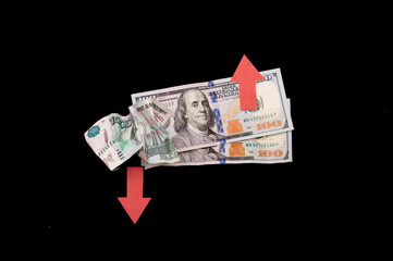 two hundred dollar bills on a black background with a red up arrow and a crumpled one thousand Russian rubles with a red down arrow on a black background. Crisis concept, falling economies