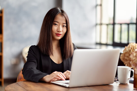 Asian business woman working in laptop in office. Japanese businesswoman work in cafe. Active serious smart female worker looking at camera