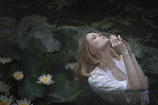 Young Blonde Woman In Dark Water With White Lilies