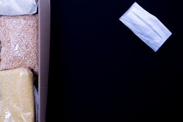 Cardboard box with Food supplies crisis food stock for quarantine and medical mask on the black background. Rice, canned food, toilet paper. Food delivery. coronavirus quarantine concept. Copyspace