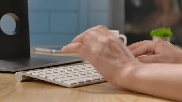 A woman is typing on a white keyboard of a computer sitting at an office table or at home. Using a computer for work, writing typing quickly or communication. Close up. Slow motion.