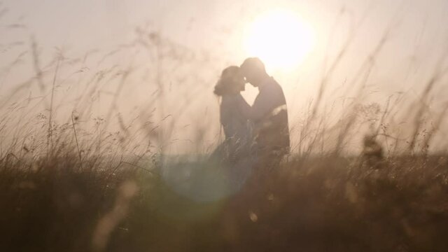 Silhouette people out of focus on the background of nature. Loving couple at sunset in nature. The grass is in the foreground. Romantic sunset. A couple of man and woman love each other. Love story.