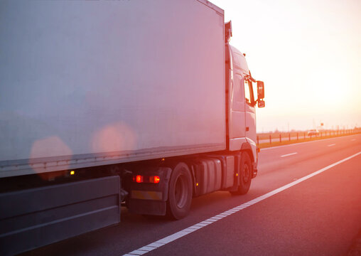 a truck with an isotherm semitrailer transports cargo along the highway against the backdrop of an evening sunset. Concept of delivery of goods, cargo transportation, copy space for text