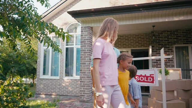family walking, giving high five and hugging near new house and sold board