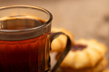 Homemade pastry cookies with jam and a faceted glass of tea in a vintage Cup holder on a background of homespun fabric with a rough texture, close-up, selective focus.