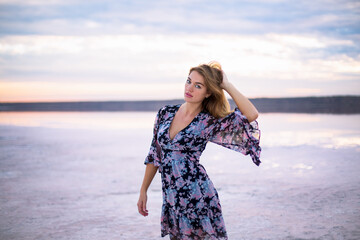 beautiful girl in a flower dress on a salty pink still water lake at a vanilla sunset