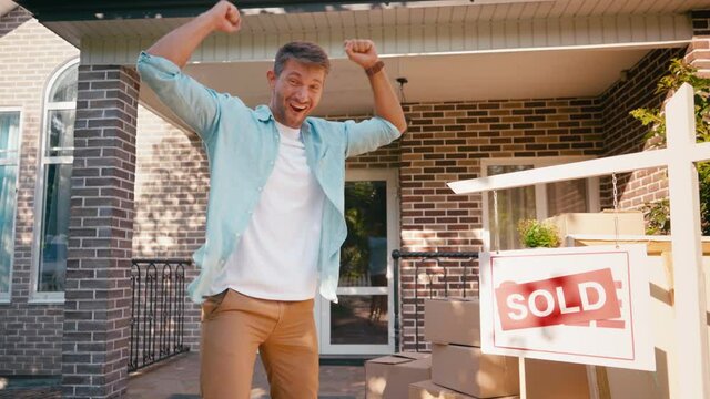 man pointing with hand at sold board, throwing boxes and jumping near house