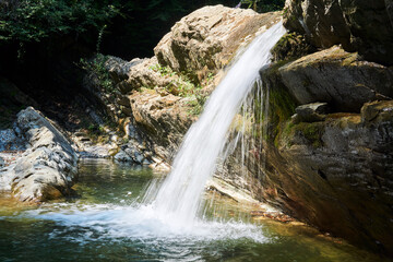small clean waterfall falls from a rocky ledge in a mountain valley