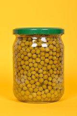 Canned green peas in a glass jar on a yellow background.