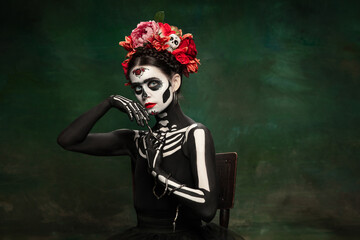 Fototapeta na wymiar Snake queen. Young girl like Santa Muerte Saint death or Sugar skull with bright make-up. Portrait isolated on dark green studio background with copyspace. Celebrating Halloween or Day of the dead.