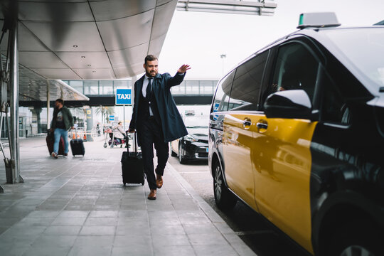 Handsome Male Passenger In Formal Outfit Waving To Yellow Cab Hurry Up To Business Meeting During Travel Trip, Caucasian Man Lawyer With Baggage Suitcase Ordering Taxi Transport At Airport Exterior