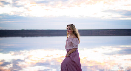 plump caucasian female in a pink dress on a pink salty still water lake at sunset