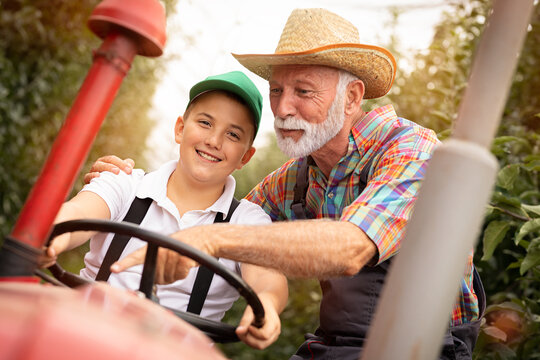 Happy Teen Boy Driving Tractor With His Grandfather